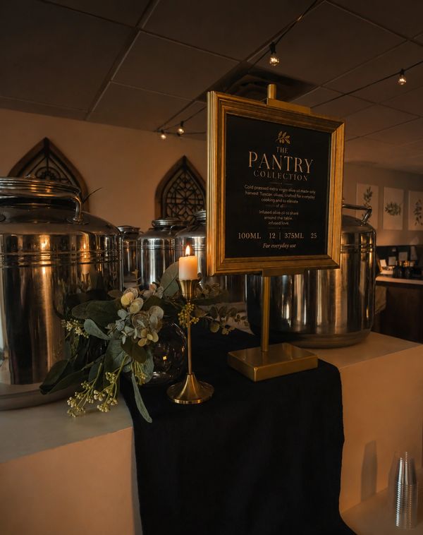 Elegant Pantry Collection display with candle and greenery on black cloth.