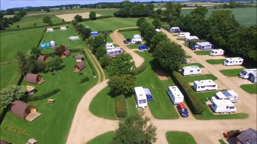 Aerial shot of campsite showing hardstanding and grass pitches and glamping pods.