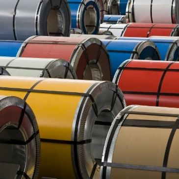 Coils of colored metal sheets stacked outdoors.