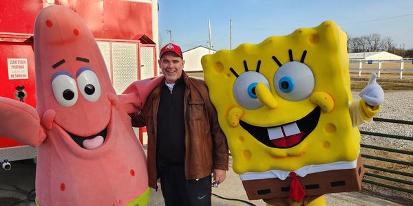 Man posing with Patrick Star and SpongeBob SquarePants mascots outdoors.