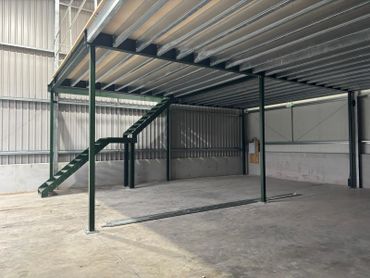 Empty industrial warehouse with metal mezzanine and stairs.