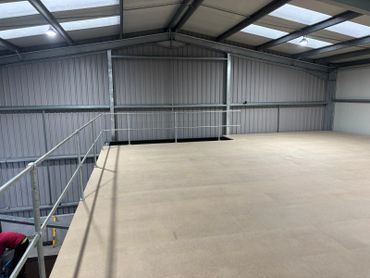 Empty industrial mezzanine floor with metal railings and skylights.