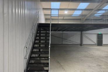Empty industrial mezzanine floor with metal stairs inside a warehouse.