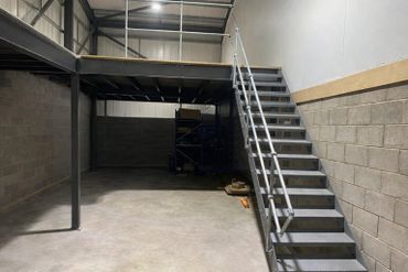 Industrial staircase leading to a mezzanine in an empty warehouse space.