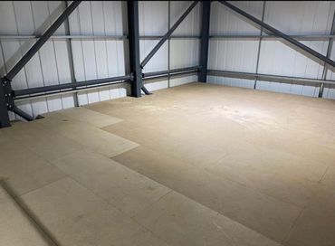 Empty indoor space with wooden flooring and metal beams.