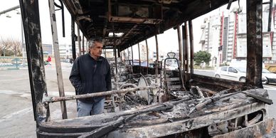 Man inspects the charred remains of a burnt-out bus.