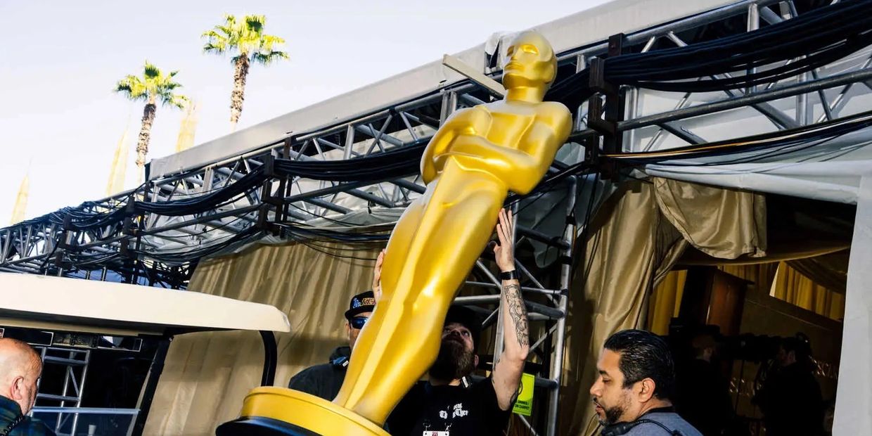 Crew setting up a large golden Oscar statue outdoors.