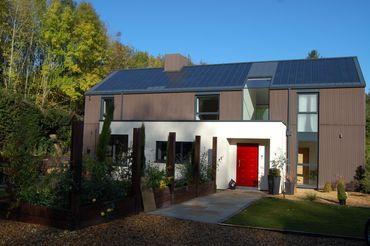 Modern house with solar panels and a red door under a clear blue sky.