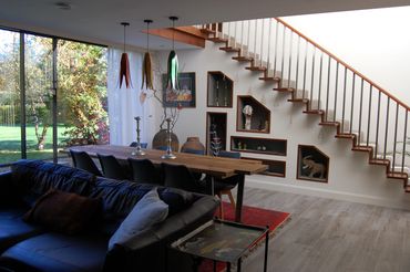 Modern living room with a wooden staircase and large windows overlooking a garden.