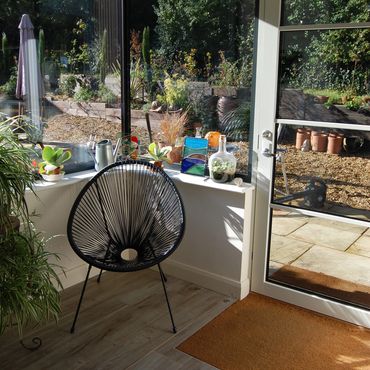 Cozy indoor corner with a black woven chair and plants by the window.