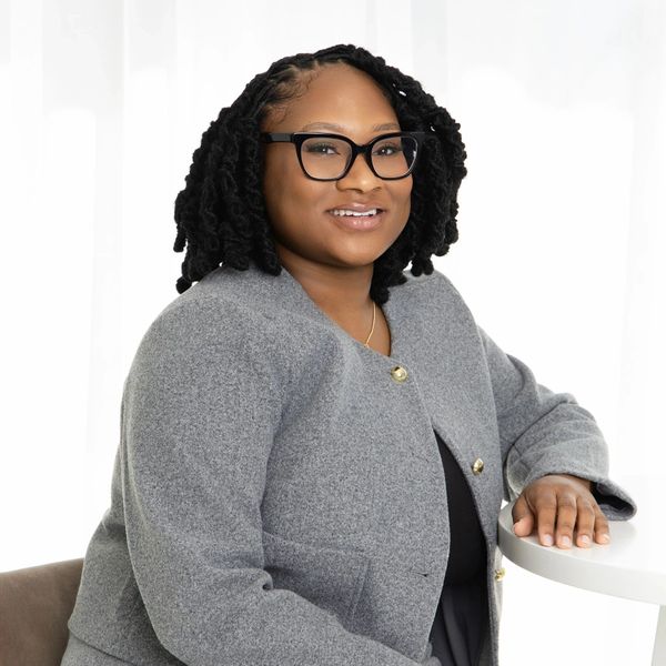 Confident woman with glasses in a gray jacket smiling at the camera.