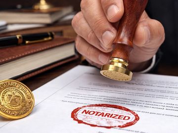 Hand stamping a document as notarized with a seal and stamp nearby.