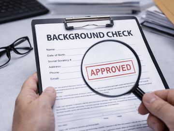 Background check form with approved stamp under magnifying glass.