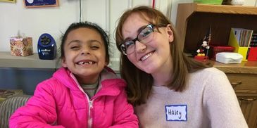 Two smiling girls, one wearing a pink jacket and the other glasses and a name tag.