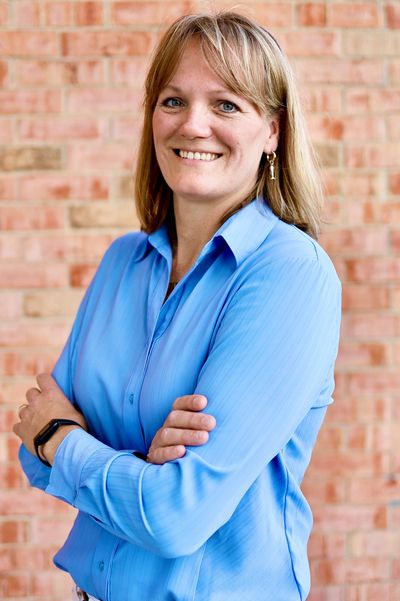 Smiling woman in blue shirt with arms crossed against a brick wall.