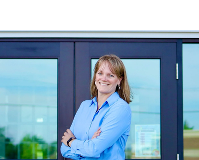 Smiling woman standing with arms crossed outside glass doors.