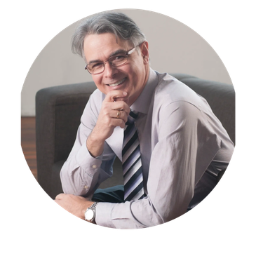 Smiling man in glasses and tie sitting on a couch.