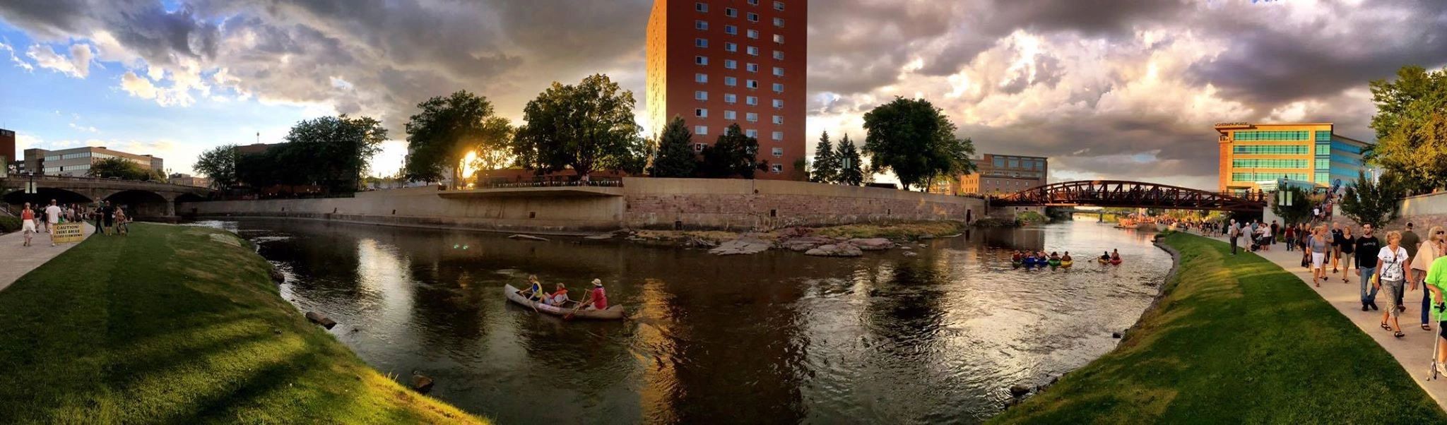 People canoeing and walking along a river at sunset in a city.