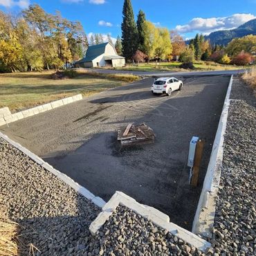 Construction site with a white car and a barn in the background.