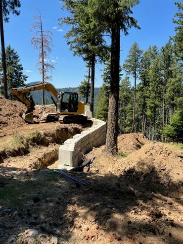 Excavator building a retaining wall in a forest.