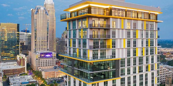 Modern high-rise building with yellow accents in a bustling cityscape at dusk.