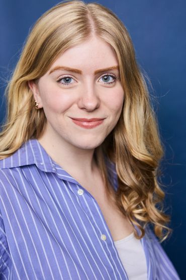 Young woman with blonde hair smiling against a blue background.