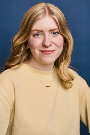Young woman with blonde hair smiling against a blue background.
