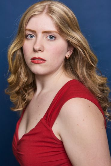 A woman with blonde hair wearing a red dress against a blue background.