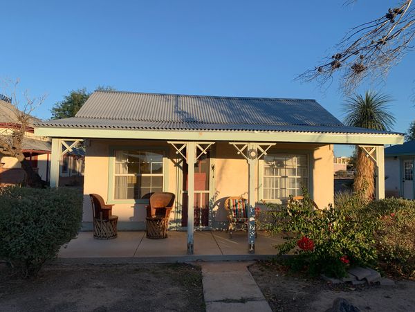 Small house with a front porch and chairs under a clear blue sky.