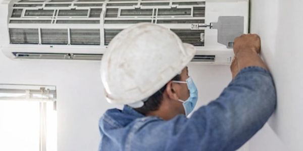 A technician in a mask and hardhat performing AC Repair in Scandia.