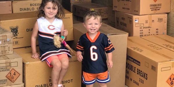 Two children posing with a Barbie doll among stacked cardboard boxes.