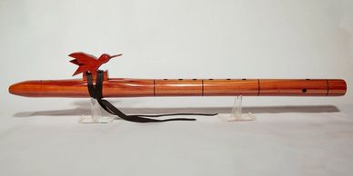 Wooden flute with a carved bird decoration and leather strap.