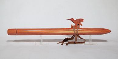 Wooden flute with a bird-shaped ornament and leather strap.