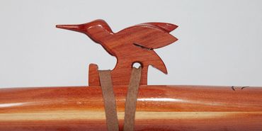 Wooden bird ornament attached to a polished wooden surface with leather straps.