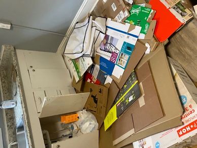 A pile of flattened cardboard boxes and paper on the floor near a wall.