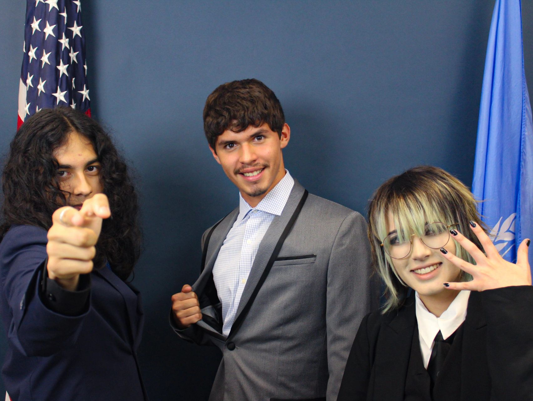 Three young people dressed in suits posing in front of flags.