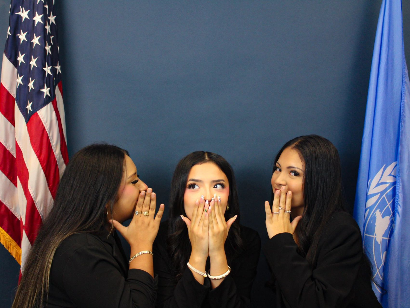 Three women whispering secrets with flags in the background.