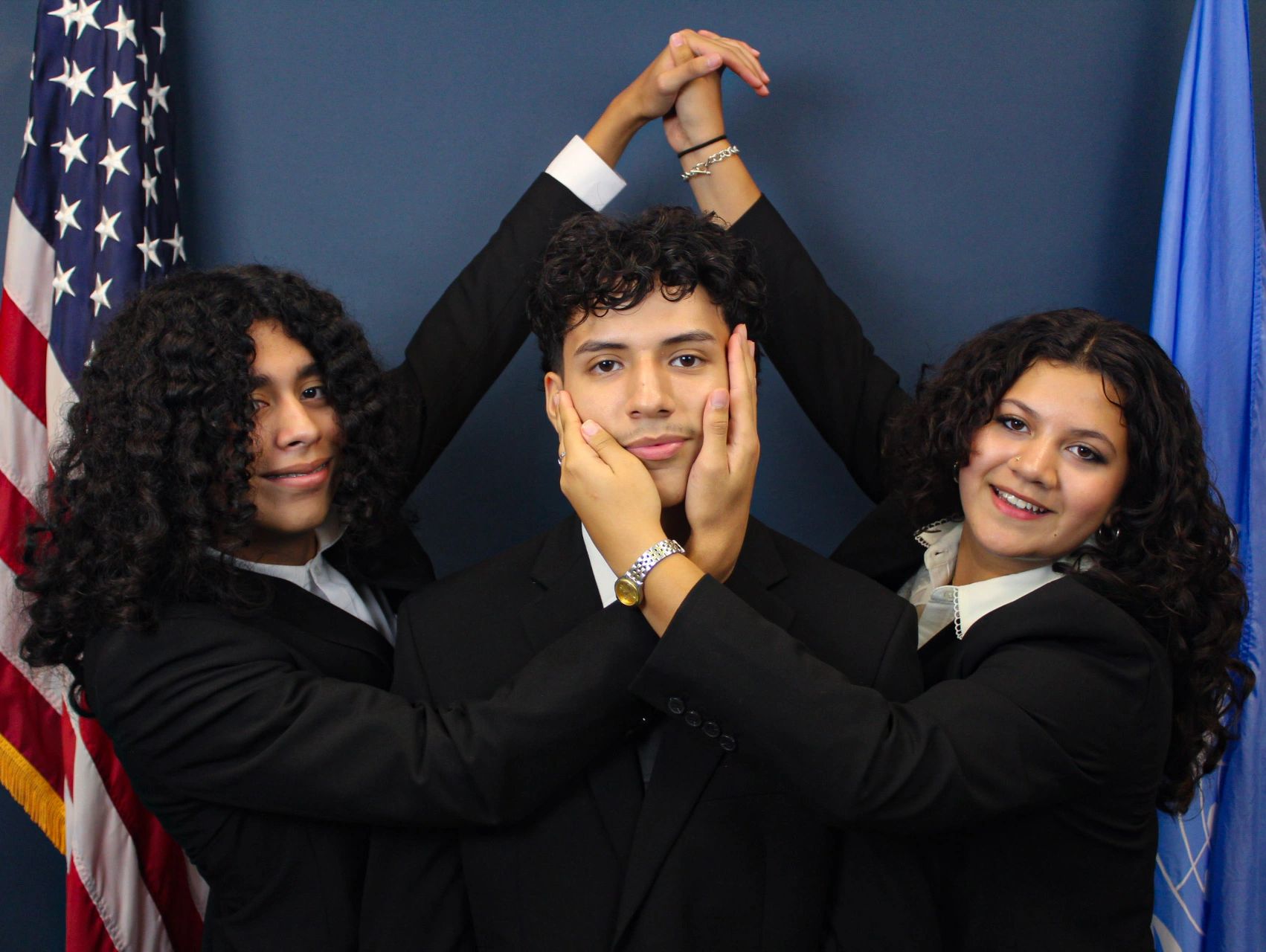 Three people in suits posing with hands joined and smiling.