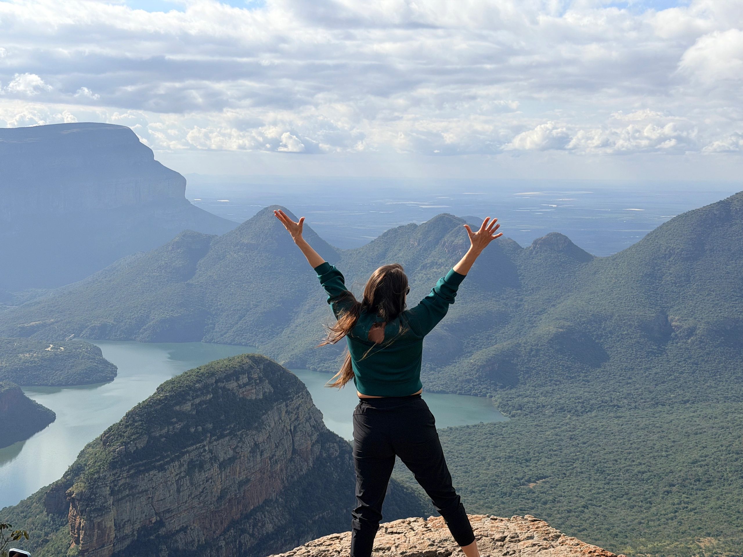 Person celebrating atop a mountain with a scenic view.