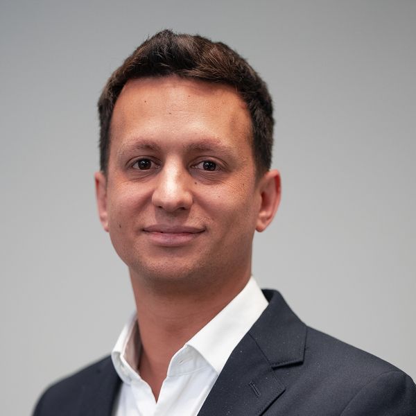 Professional man in a dark suit and white shirt against a plain background.