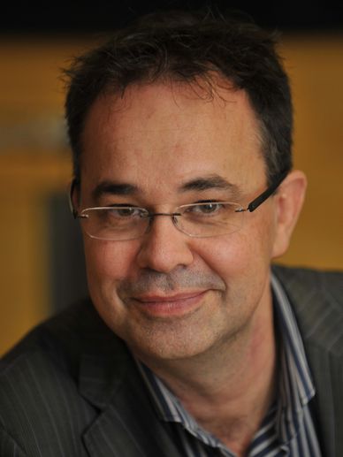 A middle-aged man with glasses smiling gently.