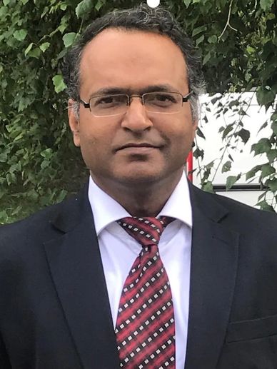 Man in a suit with glasses and a patterned tie outdoors.