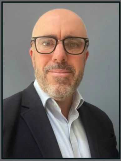 Portrait of a bald man with glasses in a suit and white shirt.