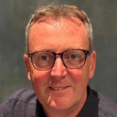 Portrait of a middle-aged man wearing glasses and a dark shirt.