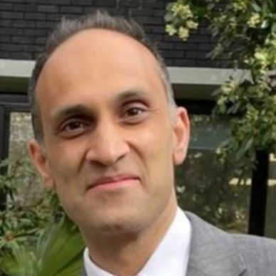 A man in a gray suit smiling outdoors.