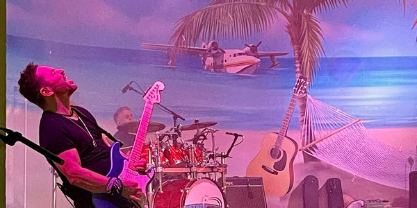 Musician passionately playing electric guitar on tropical-themed stage.