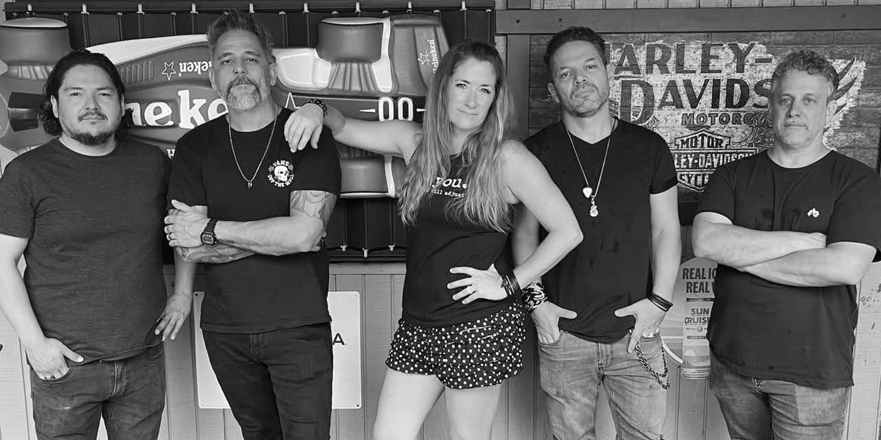 Group of five people posing in front of a Harley-Davidson sign.