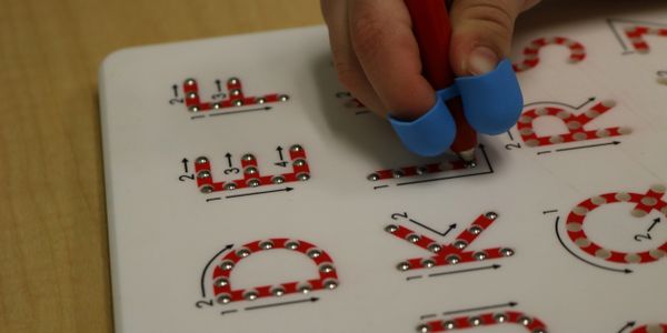 Child's hand using a pencil grip while working on writing during occupational therapy.