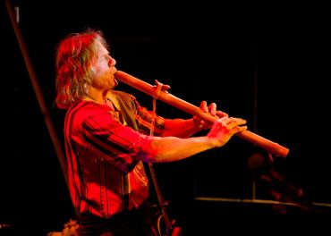Musician playing a wooden flute on stage.