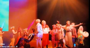 Group of people joyfully dancing on stage with vibrant lighting.